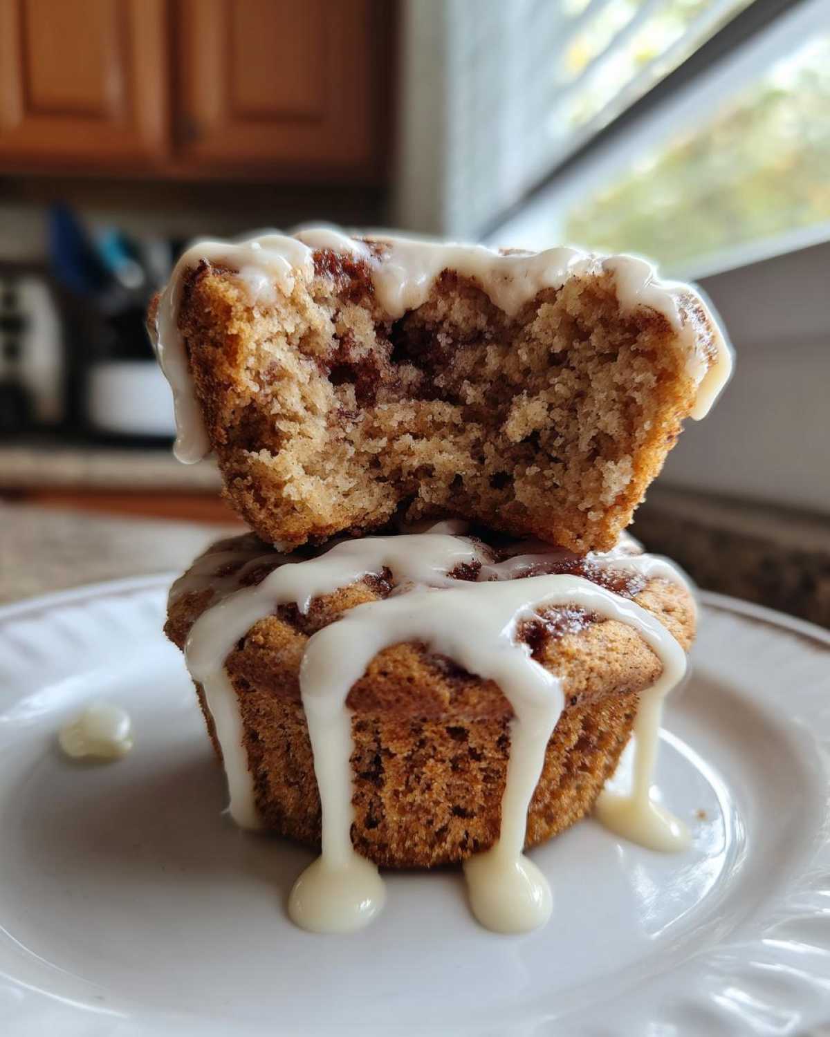 Two stacked Cinnamon Roll Muffins, one broken open to show the swirl, dripping with white glaze.