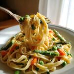 A fork lifting creamy Pasta Primavera noodles mixed with bright green peas and asparagus spears.