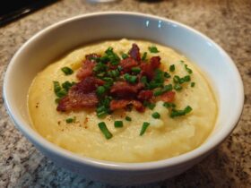A bowl of thick, creamy potato soup topped generously with crispy bacon bits and fresh chopped chives.
