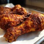 Close-up of several golden-brown, crispy Baked Chicken Legs resting on parchment paper on a metal tray.