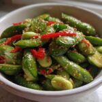 A close-up shot of a vibrant Edamame and Cucumber Salad tossed in a sesame dressing, featuring bright red pepper strips.