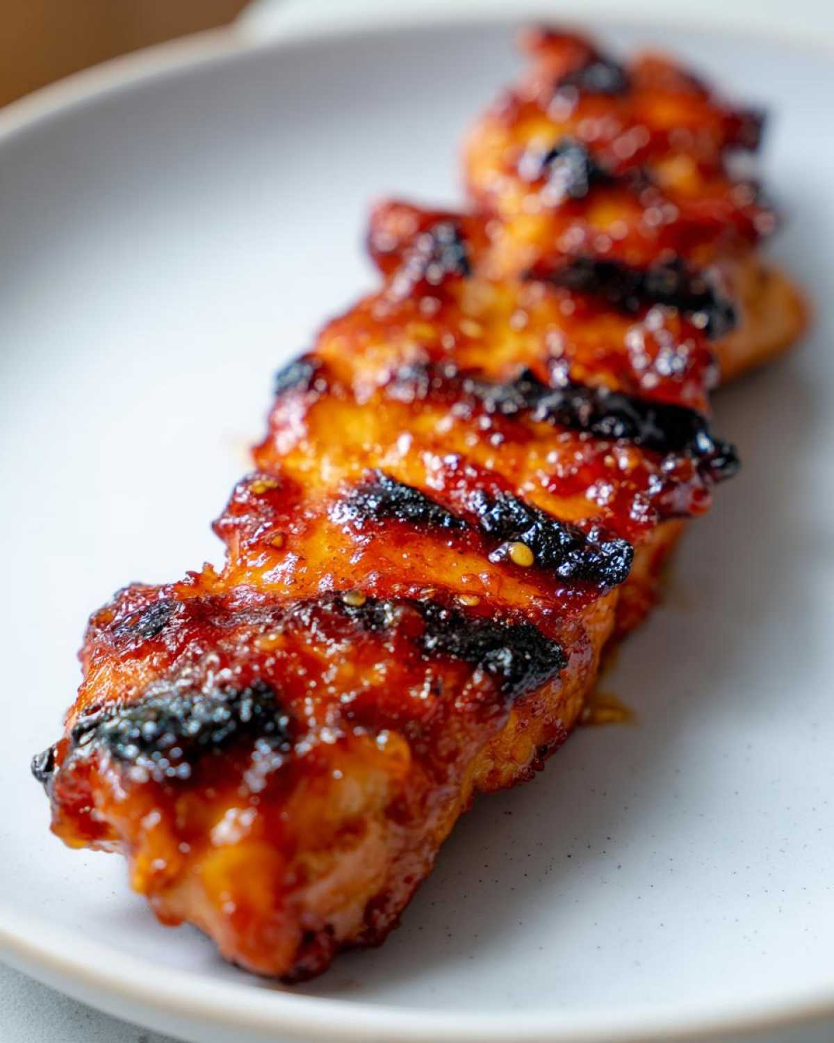 Close-up of a piece of Grilled Hot Honey Chicken, showing a shiny, caramelized glaze and distinct char marks.