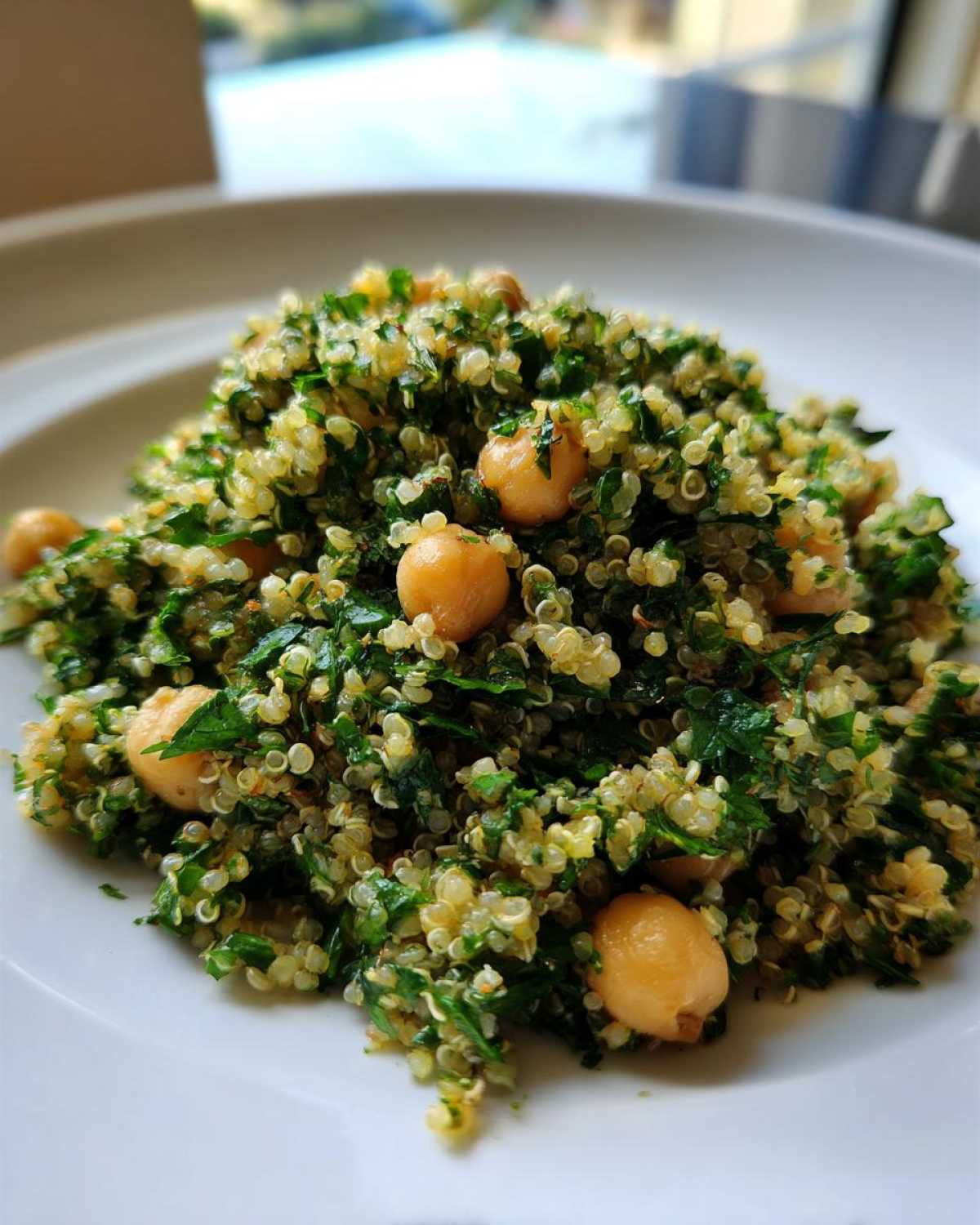 A close-up of the healthy Jennifer Aniston Salad featuring quinoa, chopped parsley, and whole chickpeas on a white plate.