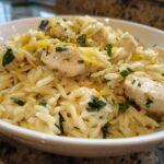 Close-up of a white bowl filled with Lemon Chicken Orzo Stir Fry, garnished with lemon zest and parsley.