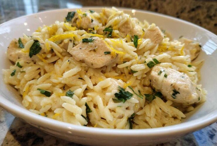 Close-up of a white bowl filled with Lemon Chicken Orzo Stir Fry, garnished with lemon zest and parsley.