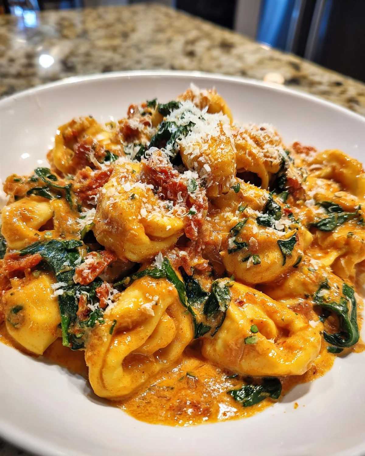 Close-up of a white bowl filled with rich Marry Me Tortellini coated in a creamy orange sauce with spinach and topped with grated Parmesan.
