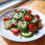 Close-up of a bright Mediterranean Cucumber Salad featuring sliced cucumbers, halved cherry tomatoes, and red onion.