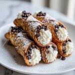 A stack of delicious Mini Cannoli Bites filled with cream, dusted with powdered sugar, and topped with mini chocolate chips.