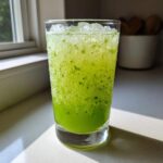 Close-up of a tall glass filled with bright green, fizzy Mint Limeade with Fresh Cucumber, topped with ice.