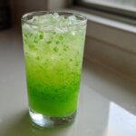 A tall glass filled with bright green, fizzy Mint Limeade with Fresh Cucumber and crushed ice.