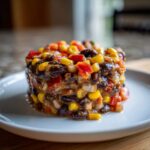 A molded serving of Dense Bean Salad featuring black beans, corn, and red peppers on a white plate.