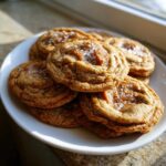 A stack of freshly baked Salted Caramel Cookies topped with gooey caramel centers and flaky sea salt.