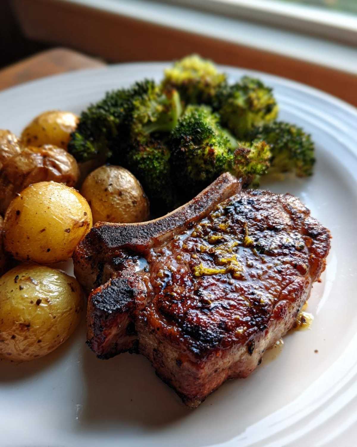 Close-up of a glazed Sheet Pan Lemon Garlic Pork Chop served with roasted potatoes and broccoli.