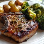 Close-up of a perfectly cooked Sheet Pan Lemon Garlic Pork Chops served with roasted broccoli and small potatoes.