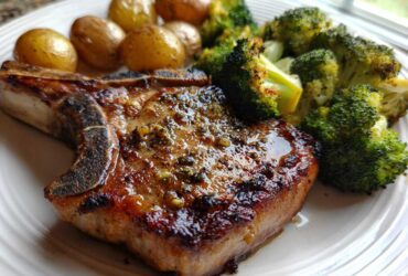 Close-up of a perfectly cooked Sheet Pan Lemon Garlic Pork Chops served with roasted broccoli and small potatoes.