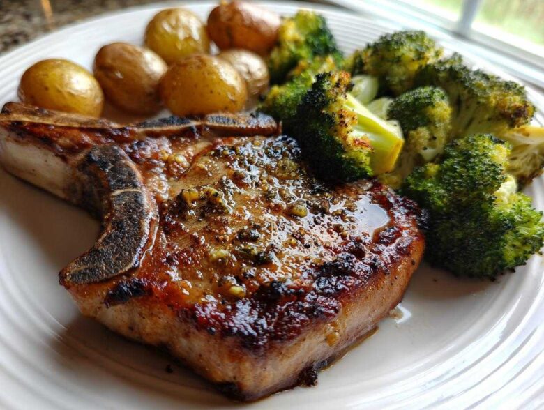 Close-up of a perfectly cooked Sheet Pan Lemon Garlic Pork Chops served with roasted broccoli and small potatoes.