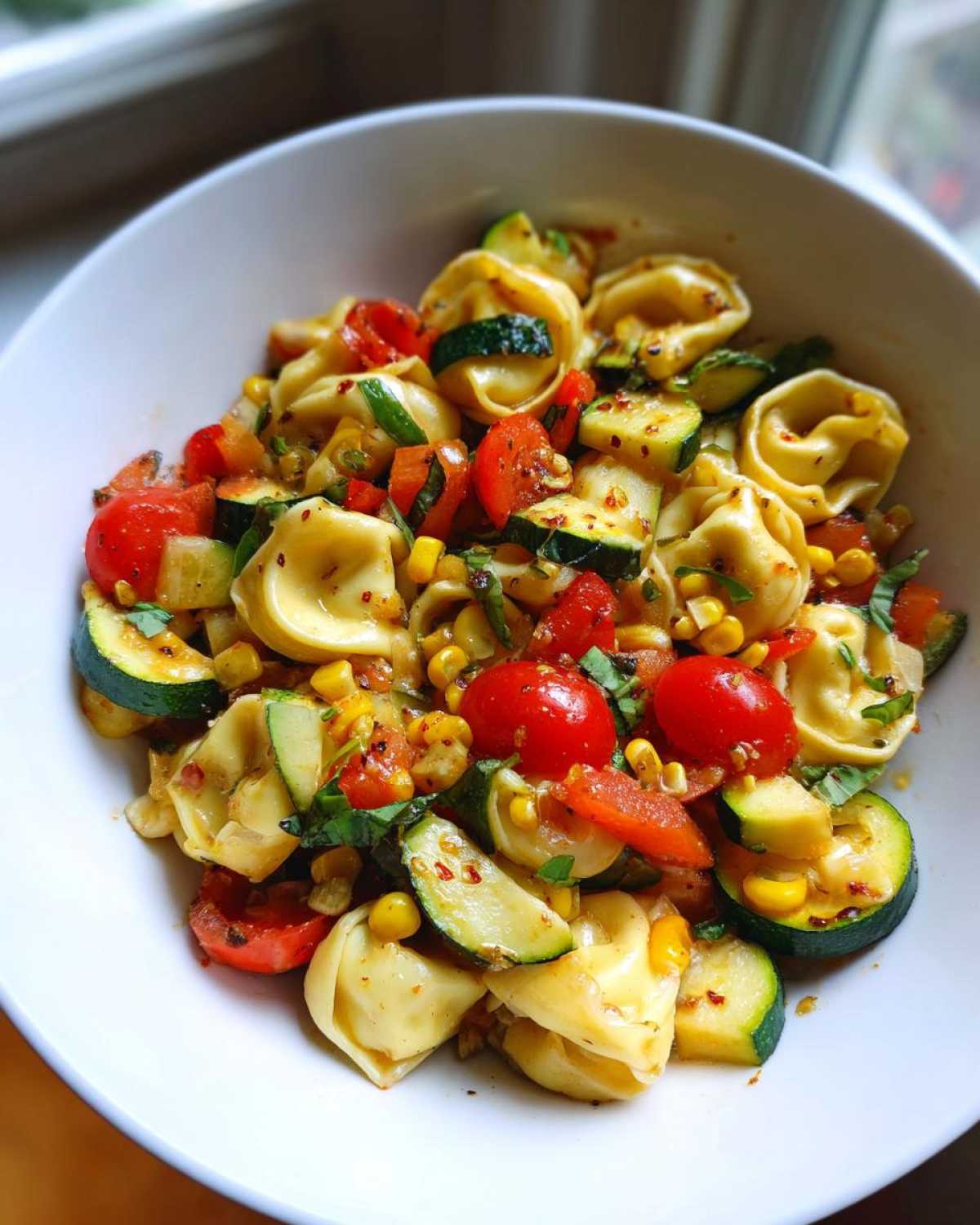 Close-up of a white bowl filled with Tortellini with Summer Veggies, featuring zucchini, cherry tomatoes, and corn.